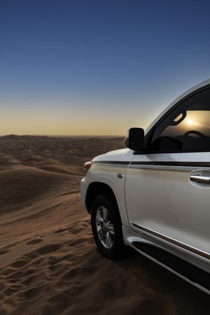 Car parked on sand dunes during sunset