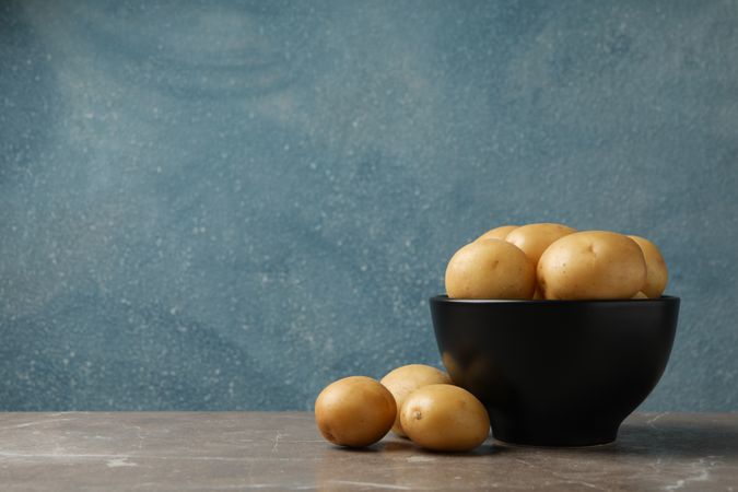 Side view of dark bowl full of potatoes, in blue room with copy space