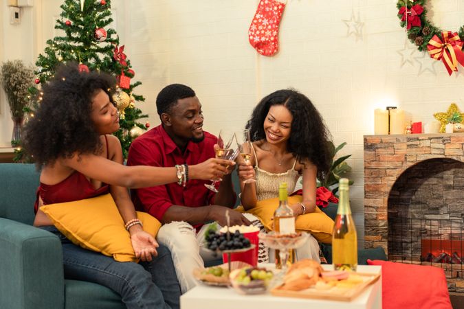 Black family with a friend are toasting with wine glasses on a sofa on Christmas
