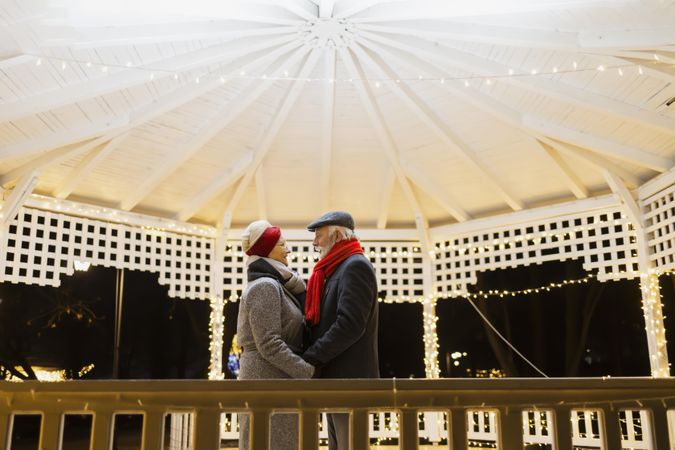 Mature couple in winter coats and scarves looking at each other under a gazebo