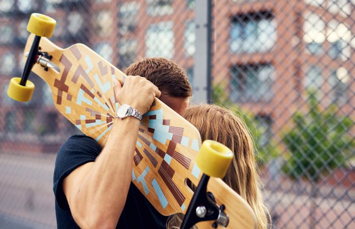 Cute couple kissing with man holding a skateboard, hiding them