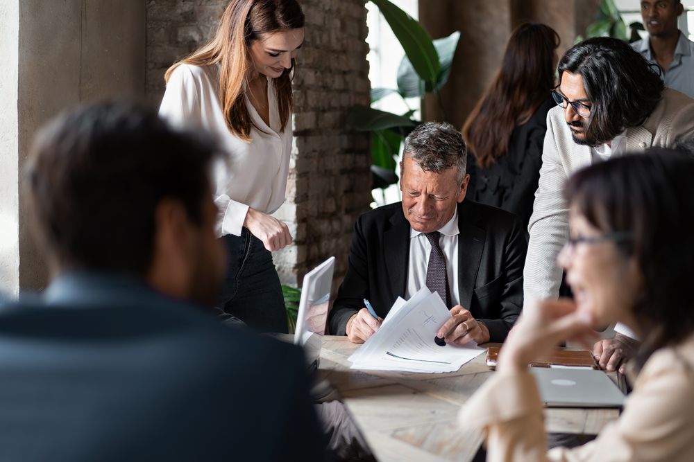 Businesspersons signing a contract together gathered around conference table