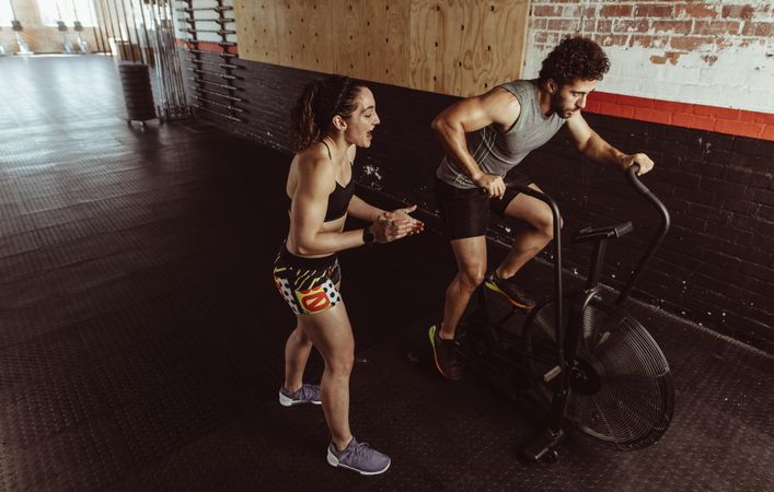 Man doing intense workout on gym bike with female coach