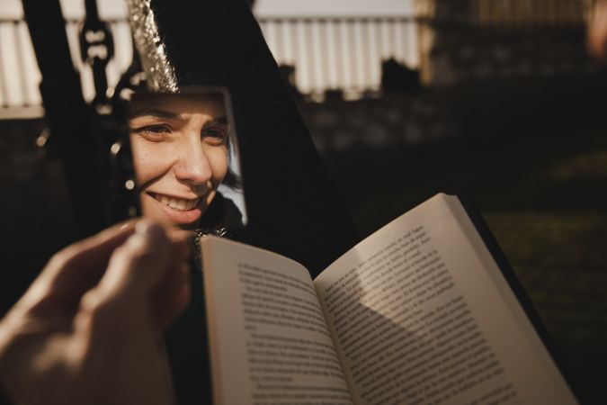 Reflection of smiling woman with book near fence