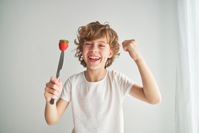 Positive boy with strawberry on top of knife