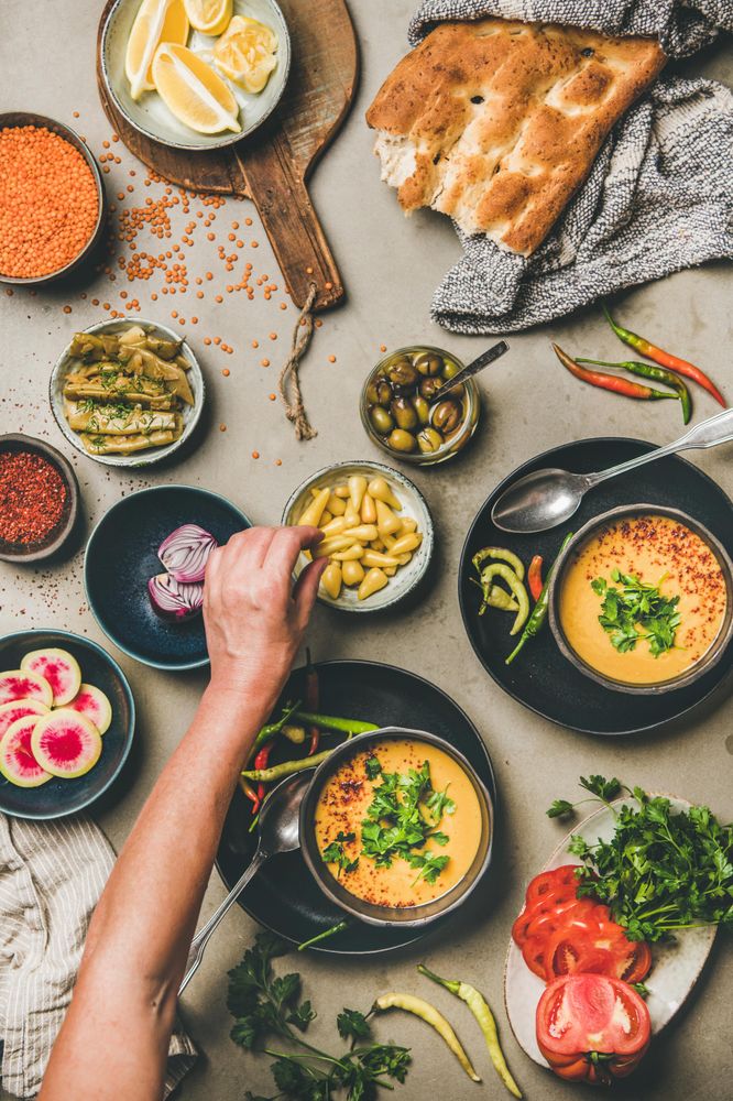 Spread of yellow lentil soup bowls, with bread, vegetable garnishes with man reaching for garnish