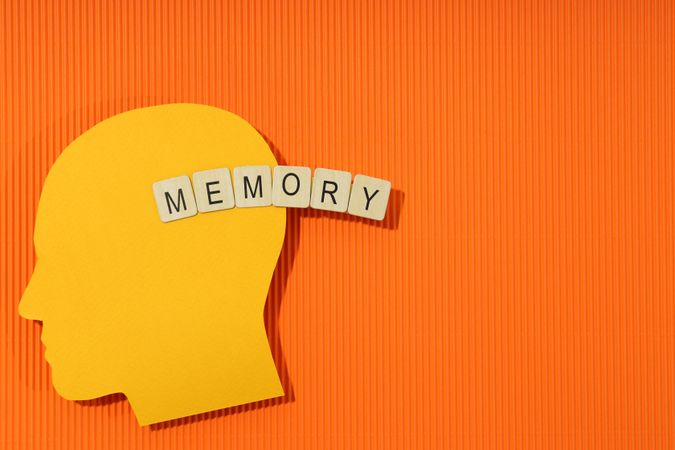 Orange duotone flat lay of head with the word “memory” in wooden blocks, space for text