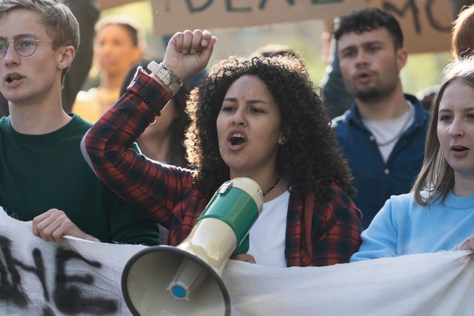Close-up of a woman with curly hair, leading a student protest using a megaphone
