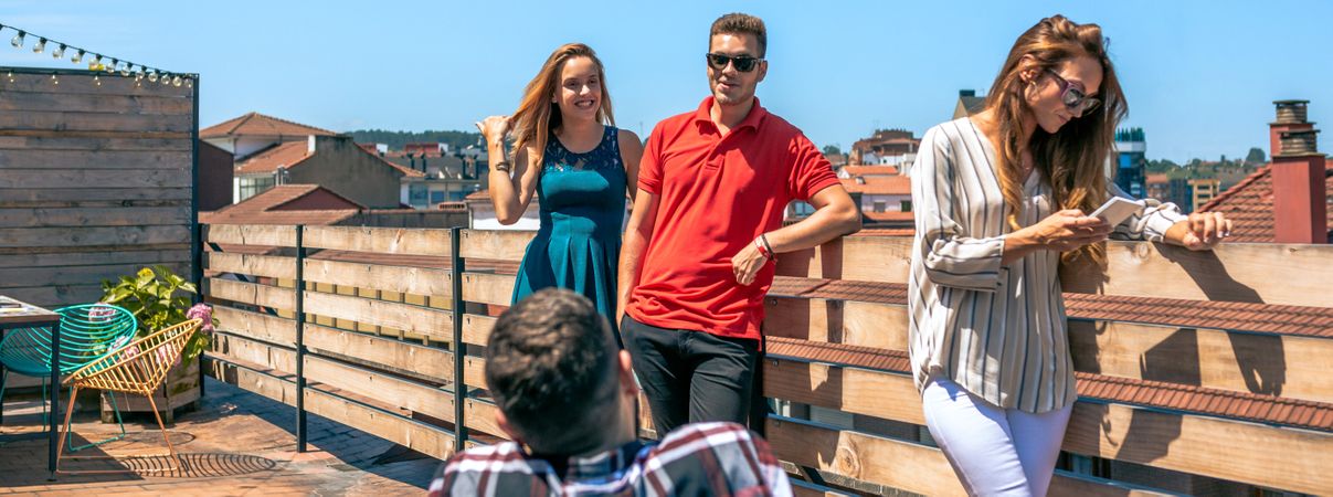 Happy friends talking in rooftop city while woman looking her phone