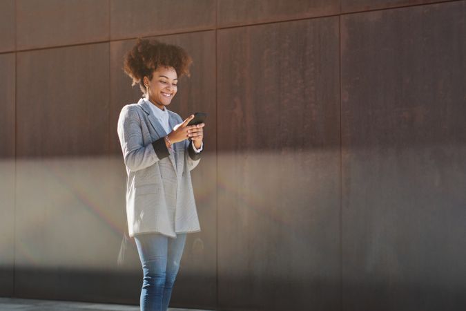 Smiling Black woman browsing smartphone on street