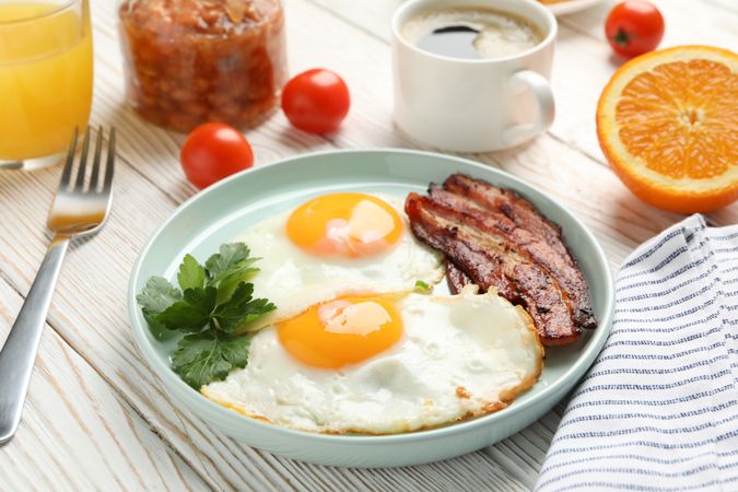 Two fried eggs sunny side up on plate with bacon with coffee