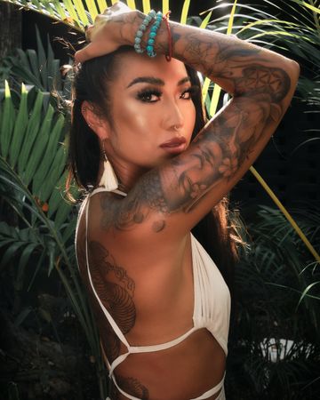 Woman with tattooed arm standing among tropical trees