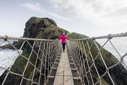Woman crossing rope bridge leading to rocky island