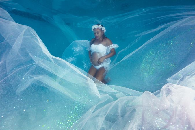 Pregnant woman in wreath and dress underwater