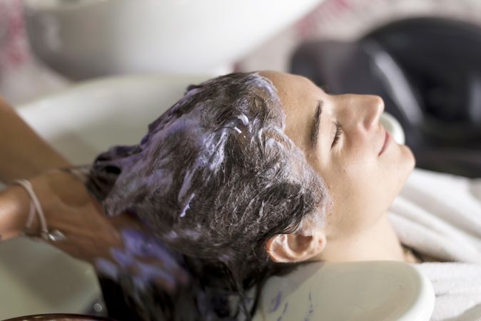 Female with eyes closed and head back in sink having shampoo massaged into her head