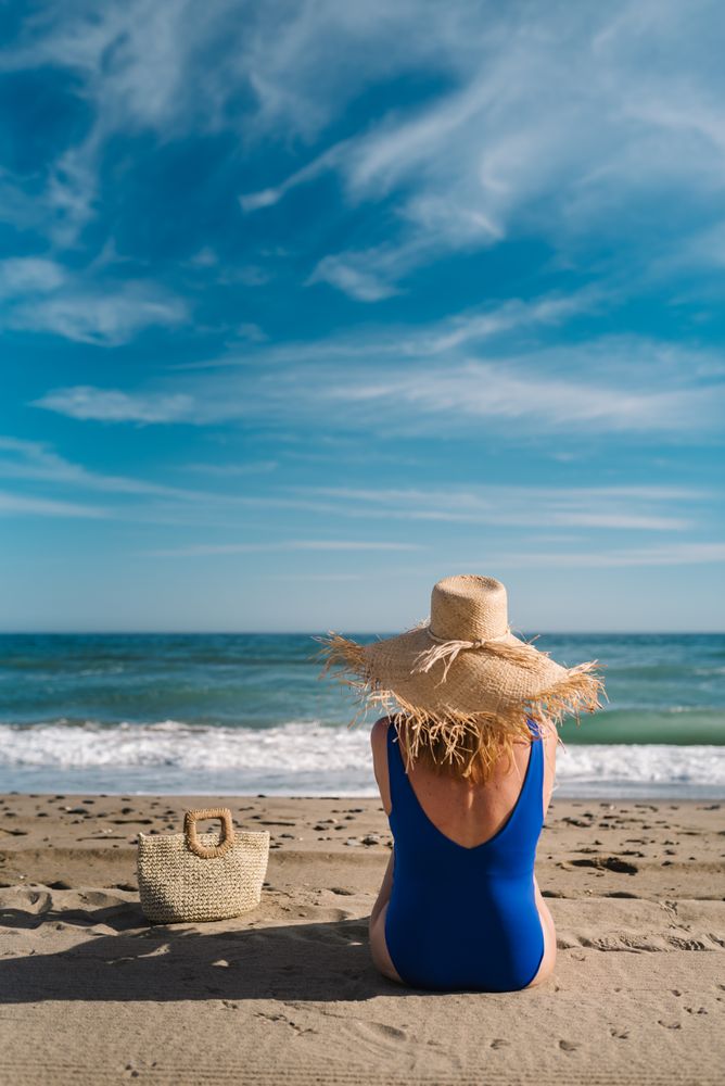 Woman in blue swimsuit and hat on sandy beach