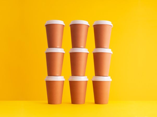 Stack of disposable coffee cups on yellow background
