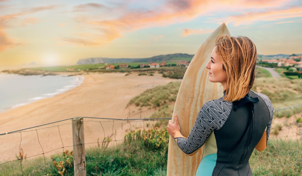 Back of female standing with surfboard atop of cliff with beautiful coastal view, banner
