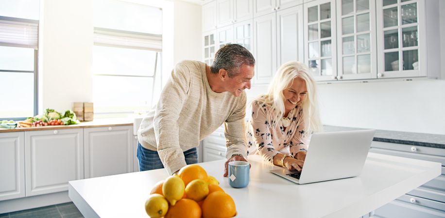 Couple looking at laptop in bright kitchen with citrus bowl