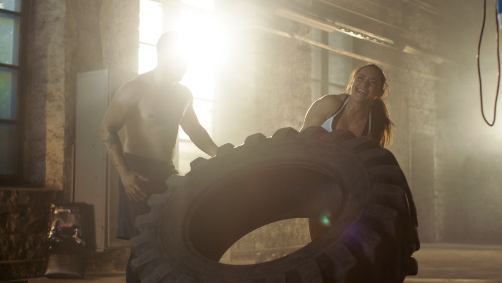 Fit Athletic Woman Lifts Tire Under Supervision of Her Partner  Trainer, as Part of Her Cross Fitness  Bodybuilding Gym Training.