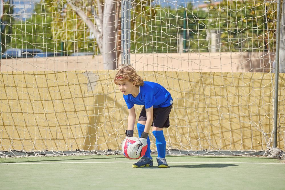 Boy standing at football goal with ball in hands