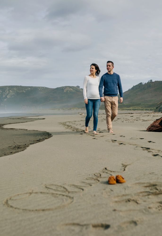 Parents to be walking with baby name Oliver written in the sand