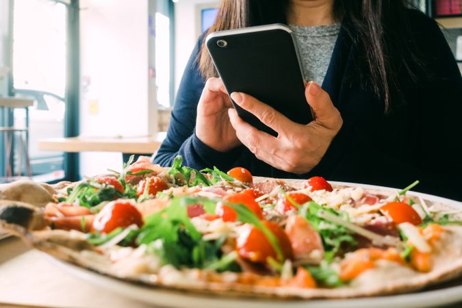 Woman with smartphone near fresh salad on table