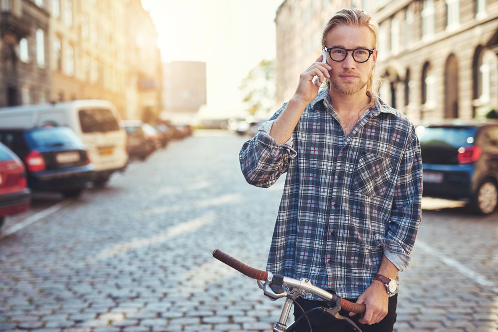 Man in glasses on his cellphone on a European cobble street with bicycle