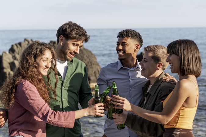 Happy diverse friends celebrating with beers by the sea during summer