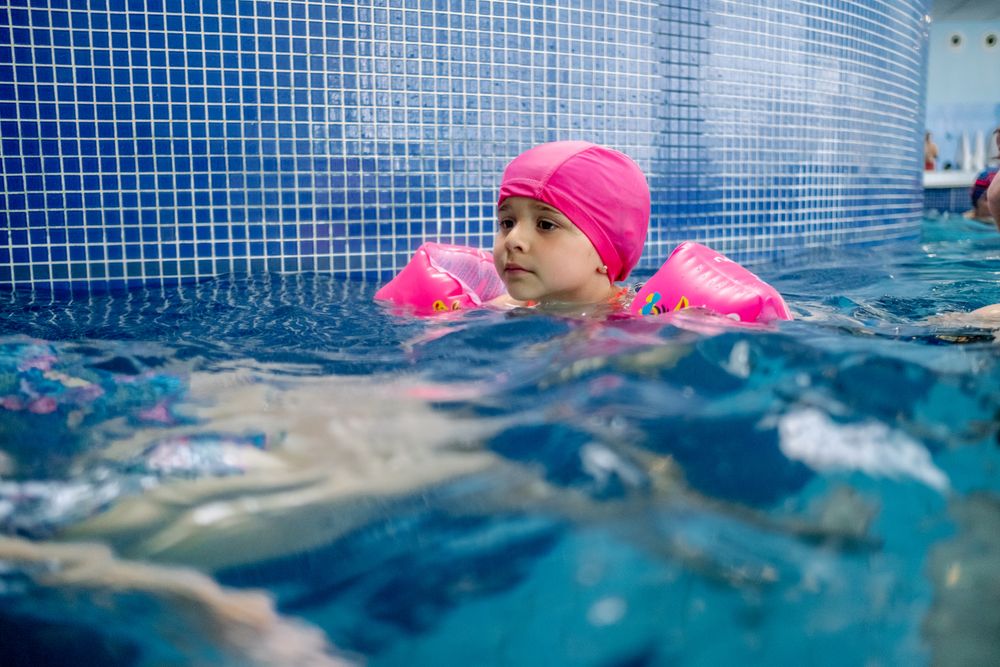 Cheerful girl in hat smiling and swimming in pool in water park