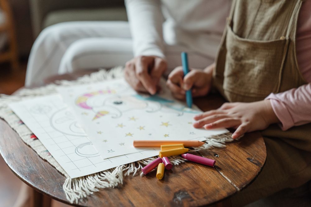 Cropped image of adult and child coloring with crayon