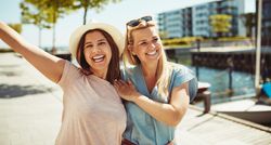 Two women laughing and holding each other on sunny day near the river