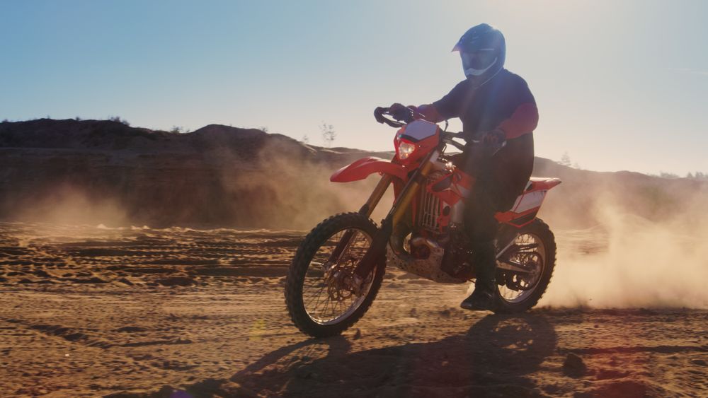 Side View Footage of the Professional Motocross Motorcycle Rider Driving on the Dune and Further Down the Off-Road Track.