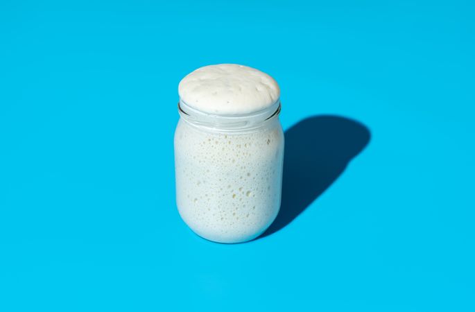 Sourdough starter in a jar, minimalist on a blue background