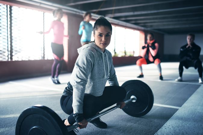 Woman about to pick up a barbell with others working out in the background