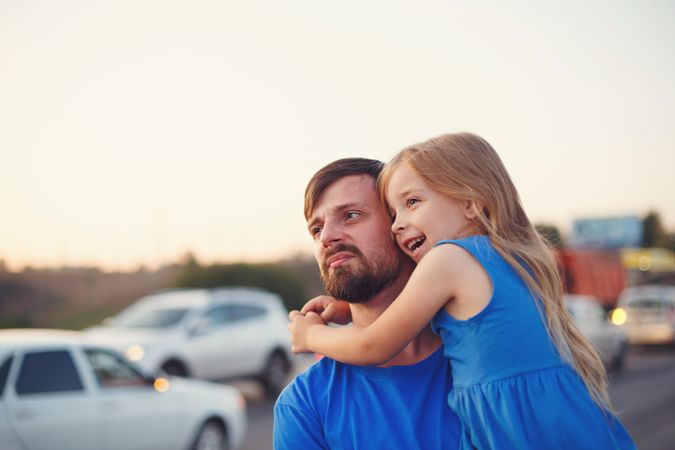 Female child being held by her father standing with cars in background
