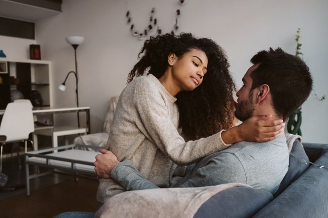 Young multiracial couple hugging on sofa