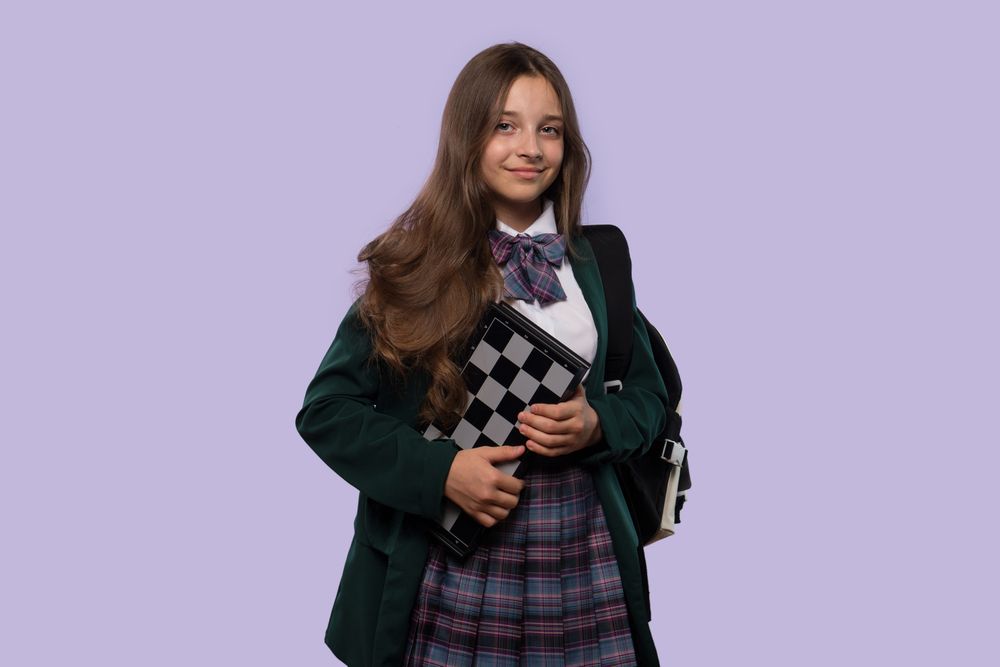Schoolgirl holds a chessboard while posing confidently.
