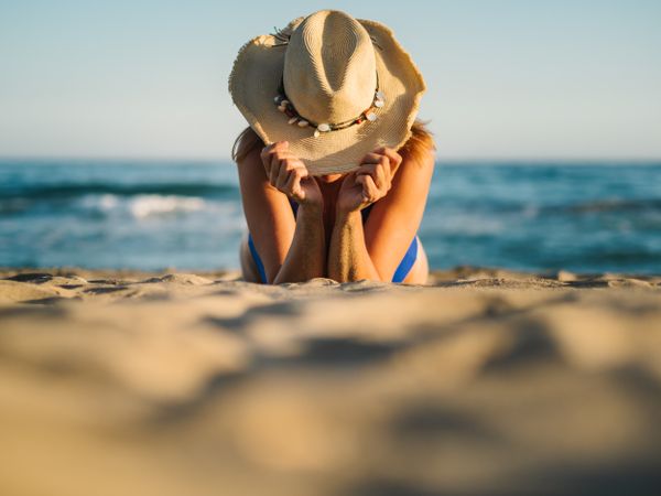 Sandy beach and woman in hat tanning