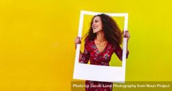Happy young woman with curly hair looking away through a blank photo frame 5zBdn5