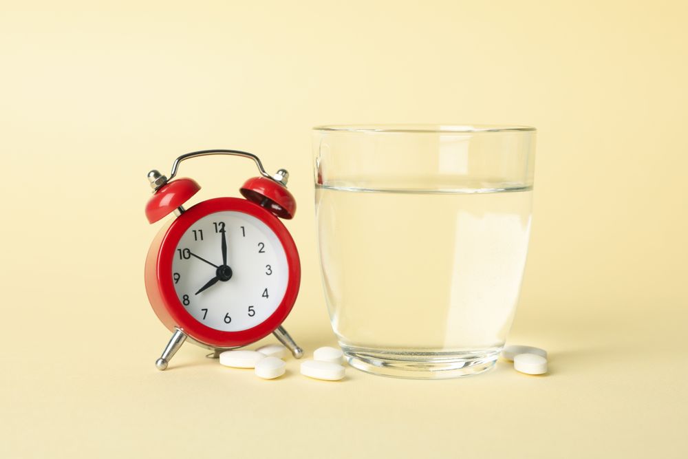 Glass of water with pills next to alarm clock in beige room