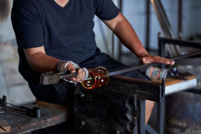 Glassblower shaping glass on rod in industry