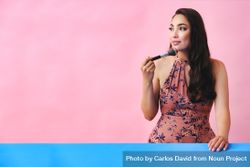 Hispanic woman with long brown hair holding large make up brush to her face, copy space bEZX10