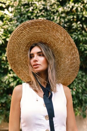 Elegant woman in straw hat standing in front of a bush