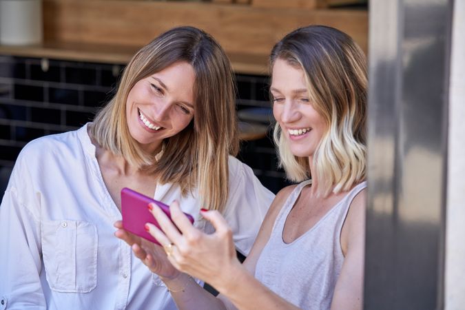 Cheerful women looking through photos on smartphone at restauran