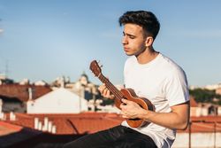 young man sitting playing ukelele on a rooftop