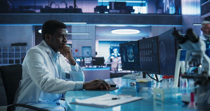 Black Male Neuroscientist Using Desktop Computer To Analyze MRI Scans Of Brain In Medical Research Center Laboratory.