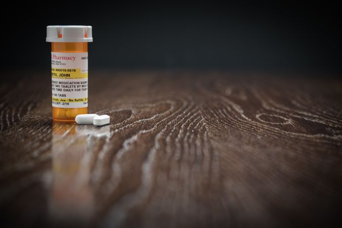 Non-Proprietary Prescription Medicine Bottle and Pills on Reflective Wooden Surface.