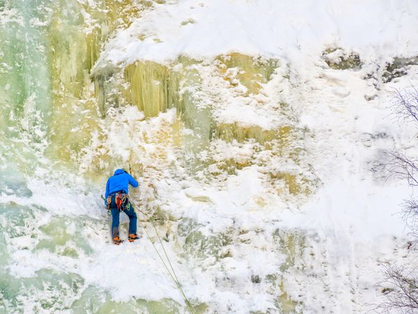Person in wintry gear scaling icy wall