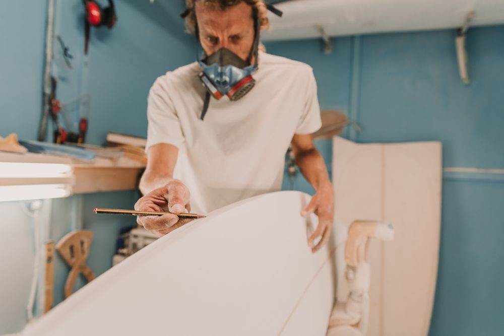 Man in respirator measuring surf board in workshop